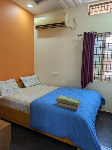 a bedroom with a bed with blue sheets and a fan at Vijayanagara Home Stay in Hampi