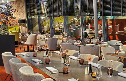 a dining room with tables and chairs and a room withwindows at Leonardo Hotel Esslingen in Esslingen