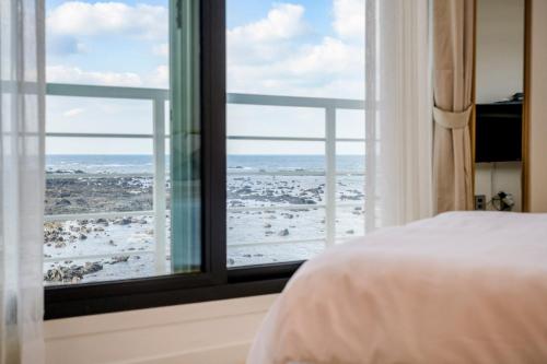a bedroom with a bed and a window with a snow covered field at On The Sea Pension in Jeju
