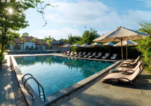 a swimming pool with lounge chairs and an umbrella at Memorina Ninh Binh Resort in Ninh Binh