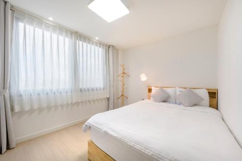 a white bedroom with a large bed and a window at On The Sea Pension in Jeju
