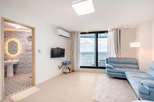 a living room with a blue couch and a bathroom at On The Sea Pension in Jeju
