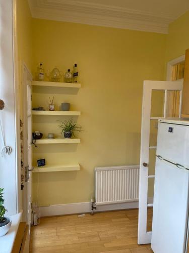 a kitchen with yellow walls and shelves and a refrigerator at 10 min to The Heart of London - Zone 2 - Charming 2 bed Apartment in London