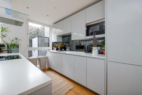 a white kitchen with white cabinets and a window at GuestReady - Modern lodge with garden in London