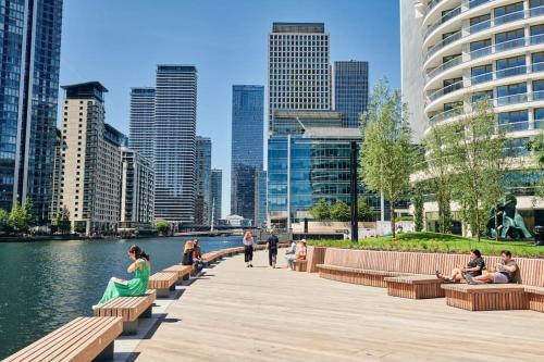 a group of people sitting on benches next to a body of water at Cosy Room by Canary Wharf in London