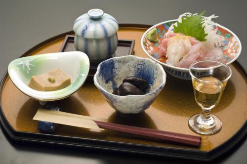 a tray with bowls of food and a glass of wine at Ekinariya Ryokan in Kusatsu