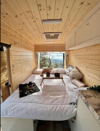 Cama grande en habitación de madera con mesa en Van Camper Ibiza MB100 Van Voyage, en Sant Carles de Peralta