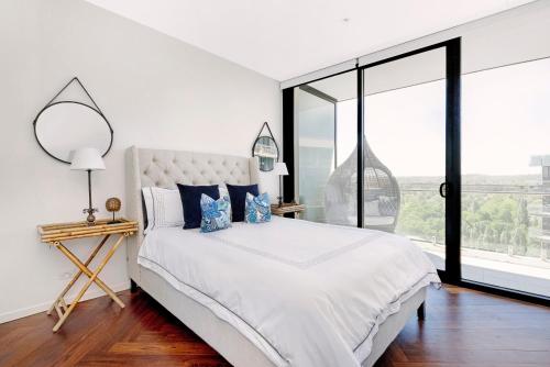 a white bedroom with a large bed and a large window at Birch Apartments in the City in Canberra