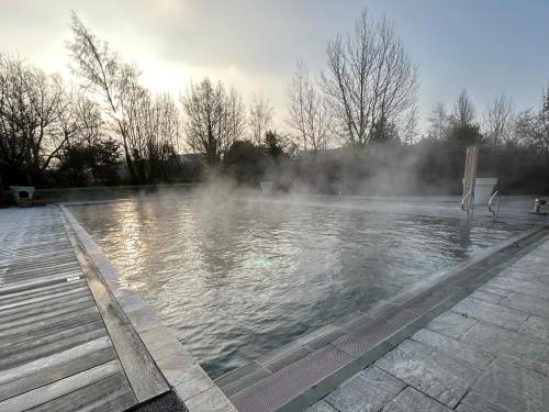 un bassin d'eau avec de la vapeur au milieu dans l'établissement Pet friendly Cotswold Cottage with hot tub and swimming pools, à Somerford Keynes
