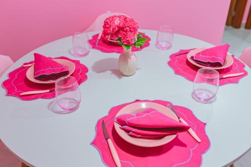 een witte tafel met roze borden en een vaas met bloemen bij Apartamento rosa in Guarapari