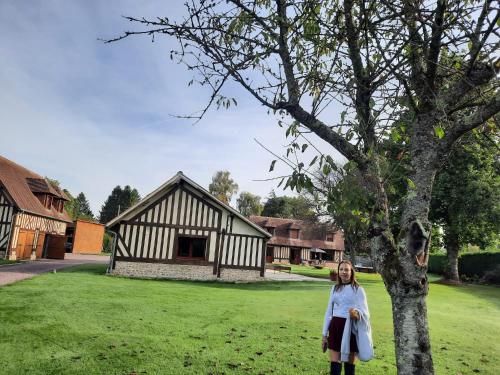 une femme debout à côté d'un arbre devant un bâtiment dans l'établissement Gite des Augettes, à Saint-Hymer