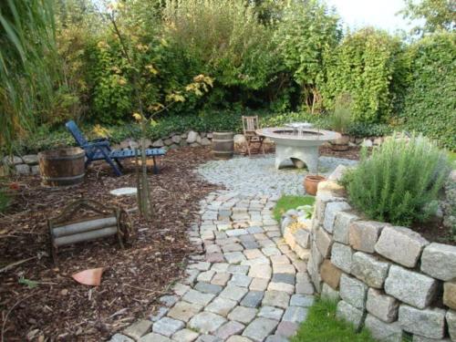 a garden with a stone wall and a bench and a table at Holiday apartment Leah in Tönning