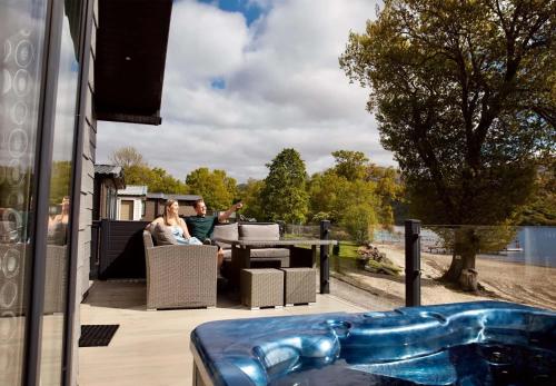 a man and woman sitting on a patio with a hot tub at Loch Lomond Holiday Park in Inversnaid