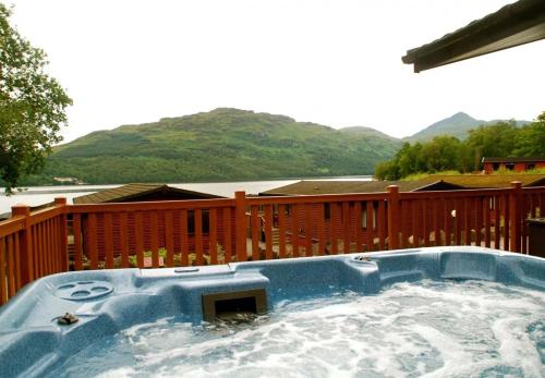 a hot tub on a deck with mountains in the background at Loch Lomond Holiday Park in Inversnaid