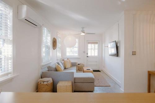 a white living room with a couch and some windows at The Bungalow Lounge by WB Abodes in Wrightsville Beach