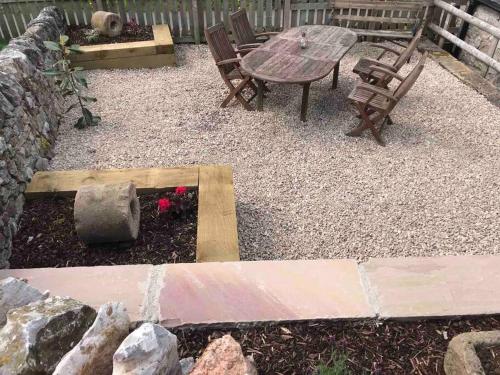 a patio with a table and chairs and a table and a stone wall at The Old Coop Barn in Brassington