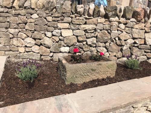a stone wall with flowers in a garden at The Old Coop Barn in Brassington