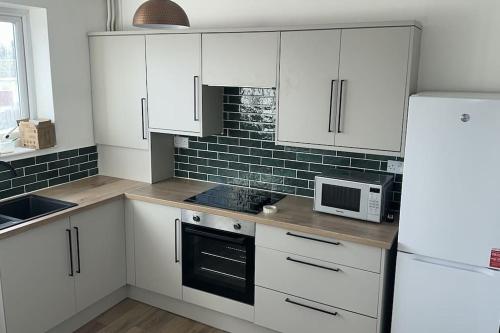 a white kitchen with white cabinets and a microwave at The Snug in Amlwch