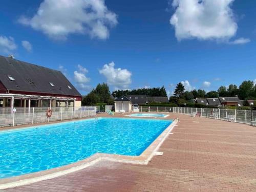 une grande piscine d'eau bleue en face d'un bâtiment dans l'établissement chalet 6 personnes avec piscine, à Cabourg