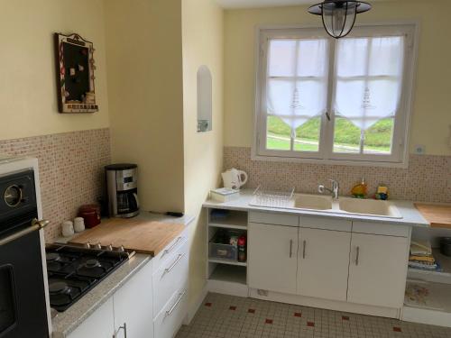 une cuisine avec des armoires blanches, un évier et une fenêtre dans l'établissement LES BAINS, à Barneville-Carteret