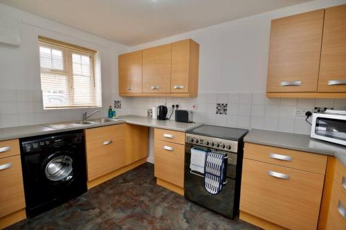 a kitchen with wooden cabinets and a black dishwasher at Highley's Nest - Fully Furnished Gem, Free Private Parking, Sky TV & Netflix in Coventry