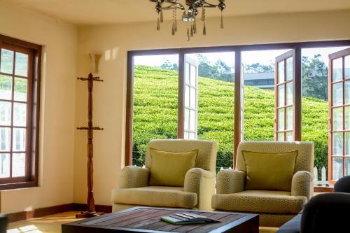 ein Wohnzimmer mit 2 Stühlen, einem Tisch und Fenstern in der Unterkunft Villa Tea Fields in Nuwara Eliya