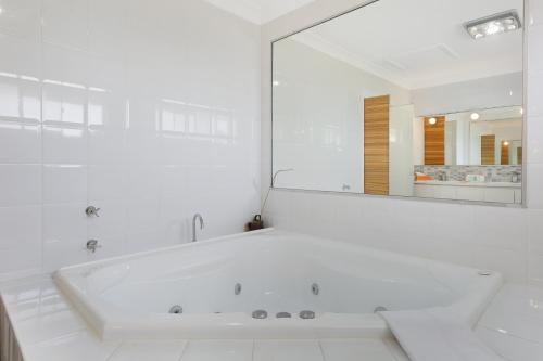 a white bathroom with a tub and a large mirror at Magnificent 4-Bed Waterfront With Pool & Views in Gold Coast