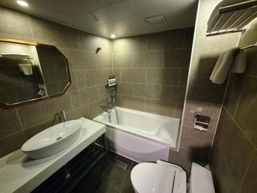No. 25 Hotel Myeongji Oceanc City Business في بوسان: حمام مع حوض وحوض استحمام ومرحاض