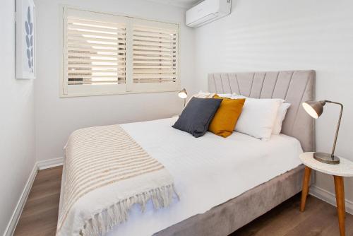 a white bedroom with a bed with pillows and a window at Cosy Unit with Parking near New Farm Park & River in Brisbane