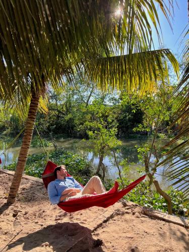 a man laying in a hammock on a beach at Sông Mê Home in Vĩnh Long