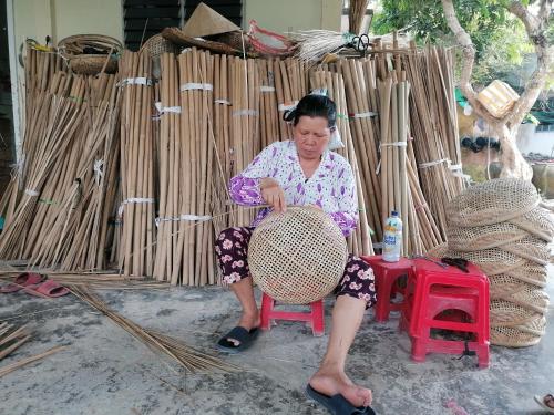 a woman sitting on a red stool in front of a wicker chair at Sông Mê Home in Vĩnh Long