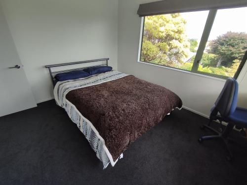 a bedroom with a bed and a chair and a window at panoramic vista with sea views in New Plymouth