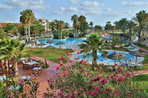 una piscina del resort con tavoli, sedie e palme di Welcome Meridiana a Taguermess