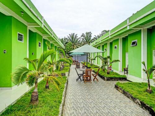un edificio verde con mesas, sillas y palmeras en OYO 92024 Green Hotel en Jambi