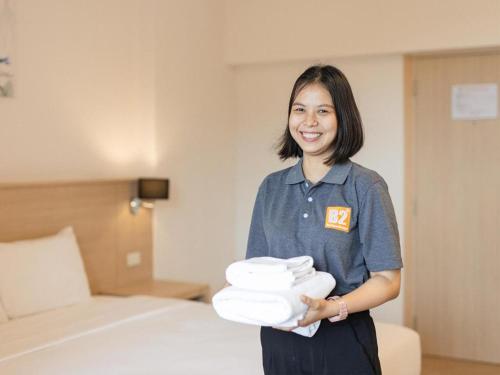 a woman holding a pile of towels in a hotel room at B2 Map Ta Phut Boutique & Budget Hotel in Ban Huai Pong
