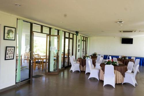 a dining room with tables and white chairs and a room with windows at Hotel Aquarium Indonesia Pangandaran in Pangandaran
