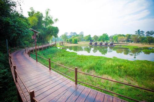 einen hölzernen Gehweg neben einem Fluss mit einem Zaun in der Unterkunft Banna Resort in Ban Na