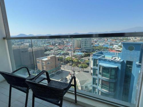 a balcony with two chairs and a view of a city at THE AVA HOTEL JEJU in Jeju