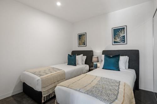 Duas camas num quarto com paredes brancas e almofadas azuis em Executive 2-Bed with Stadium View, Great Amenities em Brisbane