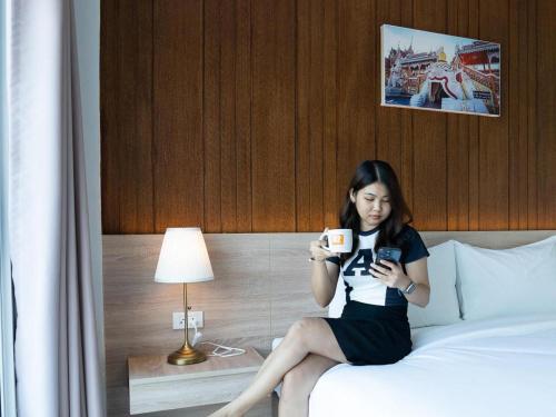 Uma mulher sentada numa cama a olhar para o telemóvel. em B2 Nakhon Sawan Boutique & Budget Hotel em Ban Nong Krot Nok