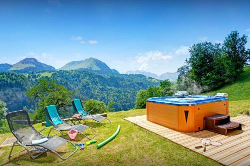 a hot tub and chairs on a deck with mountains in the background at Chalet la Croix Meridionale - OVO Network in Manigod