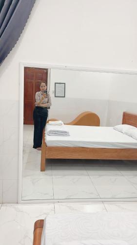 una mujer de pie junto a una cama en una habitación en Nhà Nghỉ Hạnh Phúc en Vị Thanh