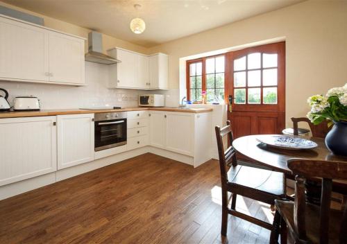 a kitchen with white cabinets and a table and a dining room at Y Betws in Abersoch