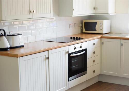 a kitchen with white cabinets and a stove and a microwave at Y Betws in Abersoch