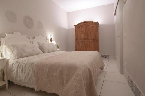 a white bedroom with a bed and a wooden cabinet at Le case del Duca in Ioppolo Giancaxio
