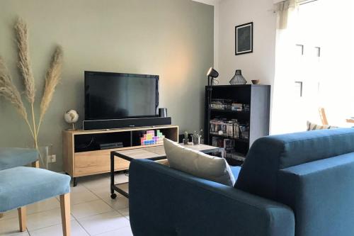 Il comprend un salon doté de 2 chaises bleues et d'une télévision à écran plat. dans l'établissement L'Amazone-Appart au calme avec balcon et parking, à Nantes