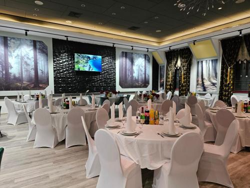 a banquet hall with white tables and chairs and a tv at Hotel Paffhausen in Wirges