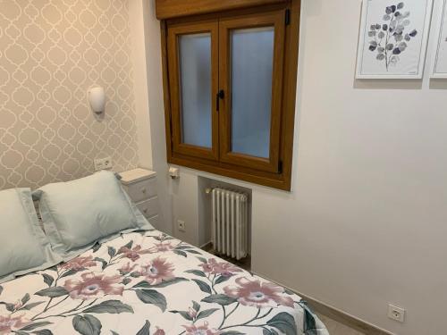 a bedroom with a bed with a floral blanket and a window at El Hogar de Belela in Oviedo