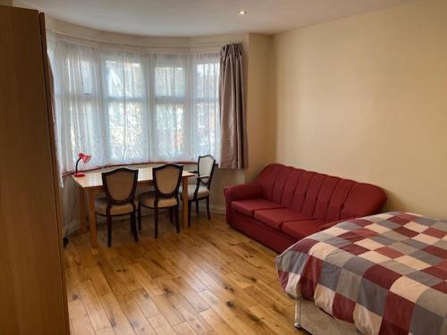 a living room with a red couch and a table and chairs at Spacious and Sunny double Room for comfortable nap in Harrow on the Hill