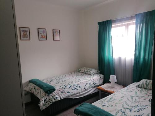 1 dormitorio con 2 camas y una ventana con cortinas verdes en Kosies Nest Gastehuis, en Ciudad del Cabo